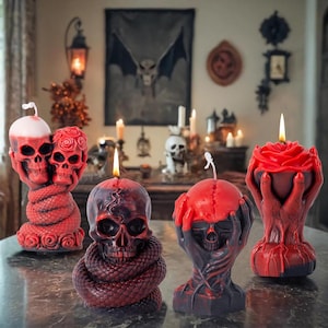 May include: A collection of Halloween-themed candles in various designs. The candles include skull shapes, a rose, and a skull entwined with a snake. The candles are red and black, with lit wicks, creating a spooky ambiance.