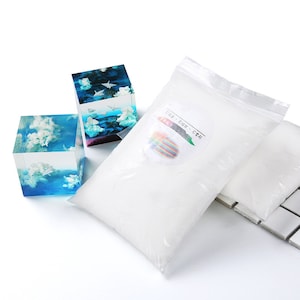 May include: Two clear resin cubes with cloud and sky designs. One cube features a blue sky with white clouds, and the other has a blue and purple sky with origami cranes. A white powder is in a clear plastic bag.