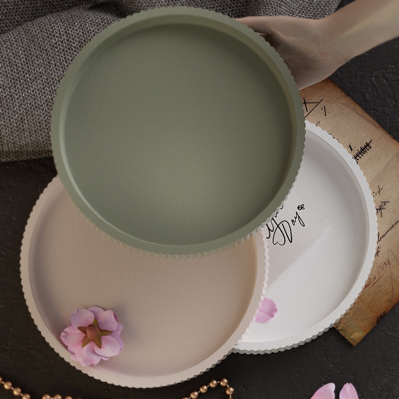 Pu&ograve; includere: Tre vassoi decorativi rotondi nei toni del verde, beige e bianco. Ogni vassoio ha un bordo smerlato. Un vassoio ha la scritta "Your Day". Sono visibili anche un fiore rosa e una collana di perline.