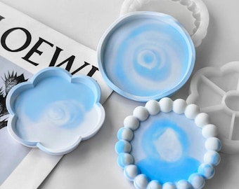 May include: A collection of resin trays in various shapes and designs. The trays feature a blue and white swirl pattern. One tray is cloud-shaped, another is round, and a third has a beaded edge. The word "LOEWE" is partially visible in the background.