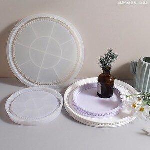 May include: A collection of round trays in various sizes. The largest tray is clear and divided into sections. A smaller clear tray and a white tray with a lavender insert are also present. A small brown bottle with greenery and a white tray with a beaded edge are also visible.