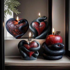 Puede incluir: Una colección de velas con forma de corazón y manzana. Las velas son rojas y negras, con una serpiente enrollada alrededor de cada una. Las velas están encendidas y las llamas son visibles. Las velas están en una estantería.