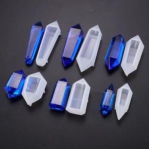 May include: An assortment of crystal-shaped molds and finished crystals. The molds are white and the crystals are a vibrant blue. The crystals and molds are arranged on a dark surface, showcasing their geometric shapes and reflective surfaces.