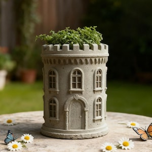 May include: A gray, castle-shaped planter with arched windows and a door. The planter is filled with green plants. The planter is sitting on a stone surface with daisies and a butterfly. The planter is a decorative garden item.