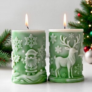 May include: Two lit green Christmas candles with white embossed designs. One candle features Santa Claus and snowflakes, the other a reindeer and bell. Festive holiday decor.