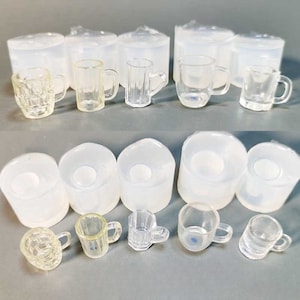 May include: A collection of small, clear glass mugs and cylindrical moulds. The mugs have different designs, some with textured patterns and others smooth. The moulds are translucent and appear to be made of silicone or a similar material.