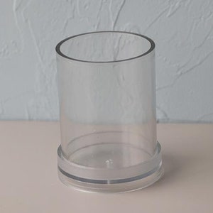 May include: A clear, cylindrical glass vase with a circular base. The vase is made of transparent glass and has a simple, modern design. The vase is approximately 5 inches tall and 3 inches in diameter.