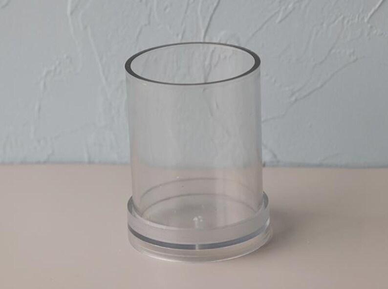 May include: A clear, cylindrical glass vase with a circular base. The vase is made of transparent glass and has a simple, modern design. The vase is approximately 5 inches tall and 3 inches in diameter.