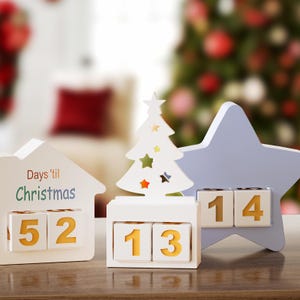 May include: A white Christmas countdown calendar with a house, tree, and star shape. The house reads "Days 'til Christmas" and displays "52". The tree shows "13" and the star shows "14". The numbers are on yellow blocks.