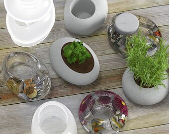 May include: An assortment of decorative items, including clear glass candle holders, stone-like planters with greenery, and a stone-like candle holder with a lit candle. The items are arranged on a wooden surface.