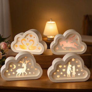 Może przedstawiać: Cztery białe lampki nocne w kształcie chmur z różnymi podświetlanymi wzorami: łabędzie, pegaz, jeleń z księżycem i gwiazdami oraz dwie postacie z gwiazdami. Światła znajdują się na drewnianej powierzchni, z lampą w tle.