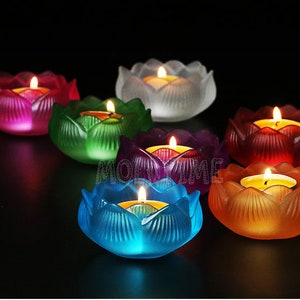 Puede incluir: Colecci&oacute;n de siete candelabros con forma de flor de loto de colores. Cada soporte es de un color diferente, incluyendo rojo, verde, morado, azul y naranja. Una vela encendida se encuentra dentro de cada soporte.