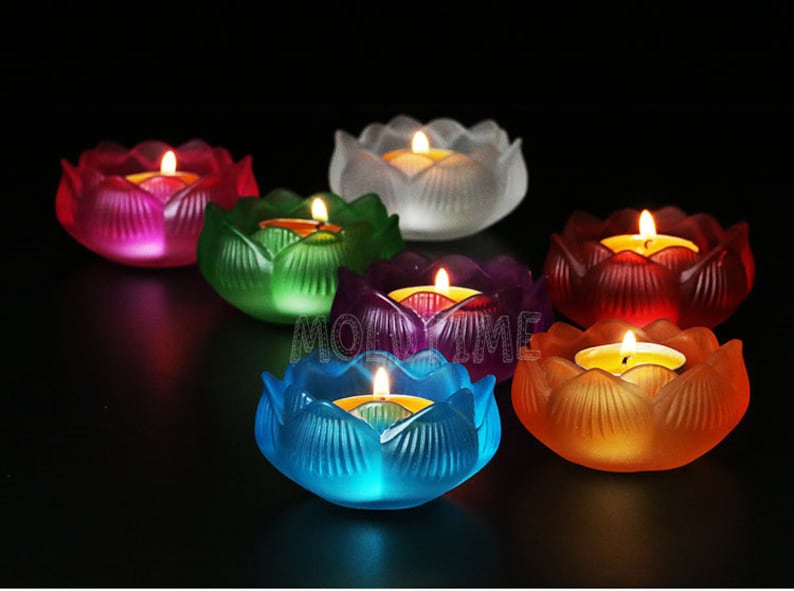 Puede incluir: Colecci&oacute;n de siete candelabros con forma de flor de loto de colores. Cada soporte es de un color diferente, incluyendo rojo, verde, morado, azul y naranja. Una vela encendida se encuentra dentro de cada soporte.
