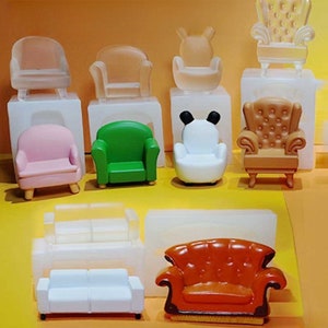 Puede incluir: Una colección de sillones y sofás en miniatura de varios colores y estilos. El surtido incluye un sillón rosa, un sillón verde, una silla blanca con orejas negras y un sillón marrón con mechones. También hay un sofá blanco y un sofá naranja.