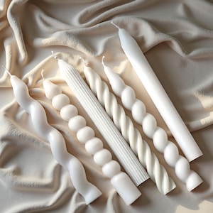 May include: A selection of white candles in different styles. The candles feature designs such as spirals, bubbles, and vertical ribs. The candles are displayed on a beige fabric, showcasing their varied shapes and textures. The candles are of different lengths.