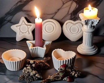 May include: A collection of white candle holders and molds in various shapes, including a star, heart, and round designs. A lit pink candle stands in a star-shaped holder, and a small candle burns atop a decorative column. Dried flowers add a touch of elegance.