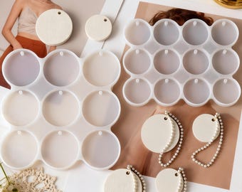 May include: A collection of craft supplies including silicone molds for making round pendants, along with finished pendants and pearl bead chains. The pendants are off-white and the molds are clear.