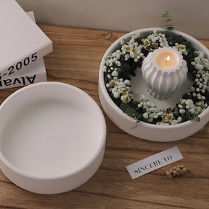 以下が含まれることがあります： 白いセラミック製のボウルが2つ。1つは空で、もう1つは花に囲まれた装飾的なホルダーに入ったキャンドルが入っています。キャンドルに火が灯っています。「SINCERE TO」というテキストが小さな白いカードに書かれています。