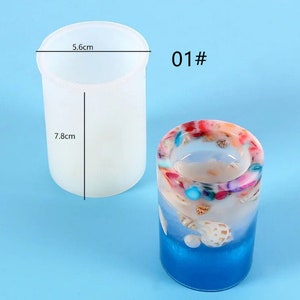 K&ouml;nnte beinhalten: Zwei zylindrische Kerzenhalter. Einer ist eine klare, schmucklose Form, 5,6 cm im Durchmesser und 7,8 cm hoch. Der andere ist ein fertiger Kerzenhalter mit blauem Sockel, wei&szlig;em und farbigem Harz und Muscheln. Der Text "01#" ist sichtbar.