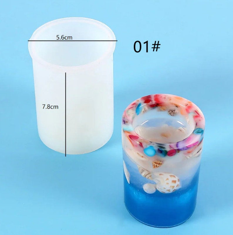 K&ouml;nnte beinhalten: Zwei zylindrische Kerzenhalter. Einer ist eine klare, schmucklose Form, 5,6 cm im Durchmesser und 7,8 cm hoch. Der andere ist ein fertiger Kerzenhalter mit blauem Sockel, wei&szlig;em und farbigem Harz und Muscheln. Der Text "01#" ist sichtbar.