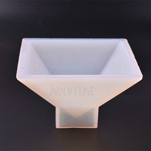 May include: A white, square-shaped silicone mold with a flared top and a rectangular base. The text "MOLDTIME" is printed in the center of the mold. The mold is designed for crafting and creating various shapes.