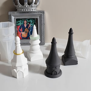 May include: An assortment of decorative tower-shaped objects in white and black, some with rings. A framed picture and a crown are in the background. The objects appear to be jewelry holders or display pieces.