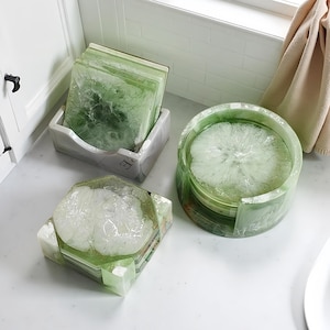 Puede incluir: Un conjunto de posavasos de resina verde y blanca en varias formas y soportes. Los posavasos tienen un aspecto veteado, con tonos de verde y blanco. Un juego es cuadrado, otro hexagonal y un tercero redondo, todos para proteger superficies.