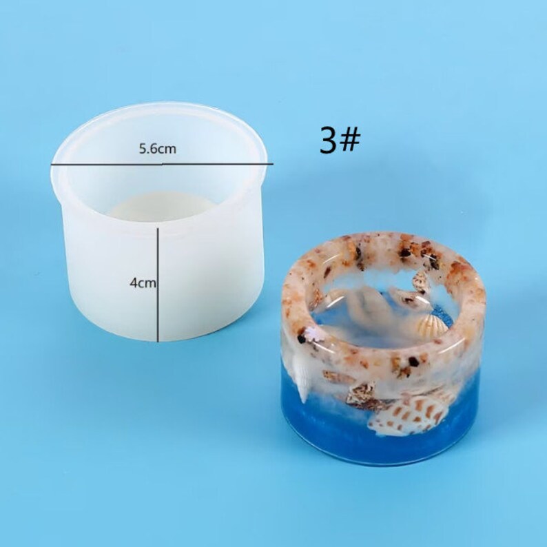 K&ouml;nnte beinhalten: Eine transparente, zylindrische Form mit 5,6 cm Durchmesser und 4 cm H&ouml;he, neben einem Harzring. Der Ring hat eine blaue Basis, eingebettete Muscheln und eine gesprenkelte, hellbraune obere Schicht. Die Nummer "3#" befindet sich oben rechts.