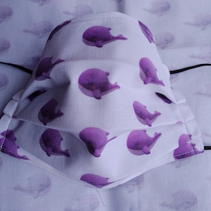 May include: White face mask with a purple whale print. The mask has pleats and is made of fabric.