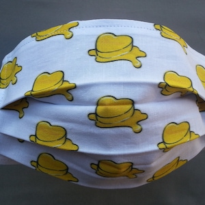 May include: White face mask with a repeating pattern of yellow melting hearts.