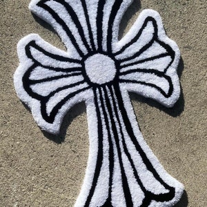 May include: White and black fluffy rug with a large cross design. The cross is outlined in black and has a white center.