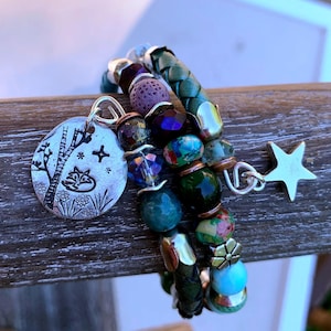May include: A multi-strand bracelet with a variety of beads in shades of green, blue, purple, and silver. The bracelet features a silver charm with a fox design, a star charm, and a braided leather band. The bracelet is approximately 7 inches in circumference.