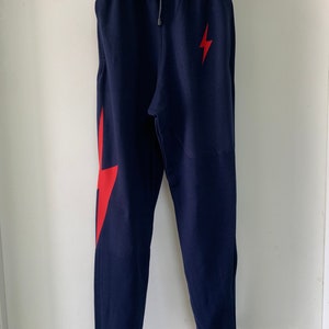 Puede incluir: Pantalones de ch&aacute;ndal azul marino con un gr&aacute;fico de rayo rojo en la pierna derecha. Los pantalones de ch&aacute;ndal tienen una cintura con cord&oacute;n y un dobladillo con pu&ntilde;os.