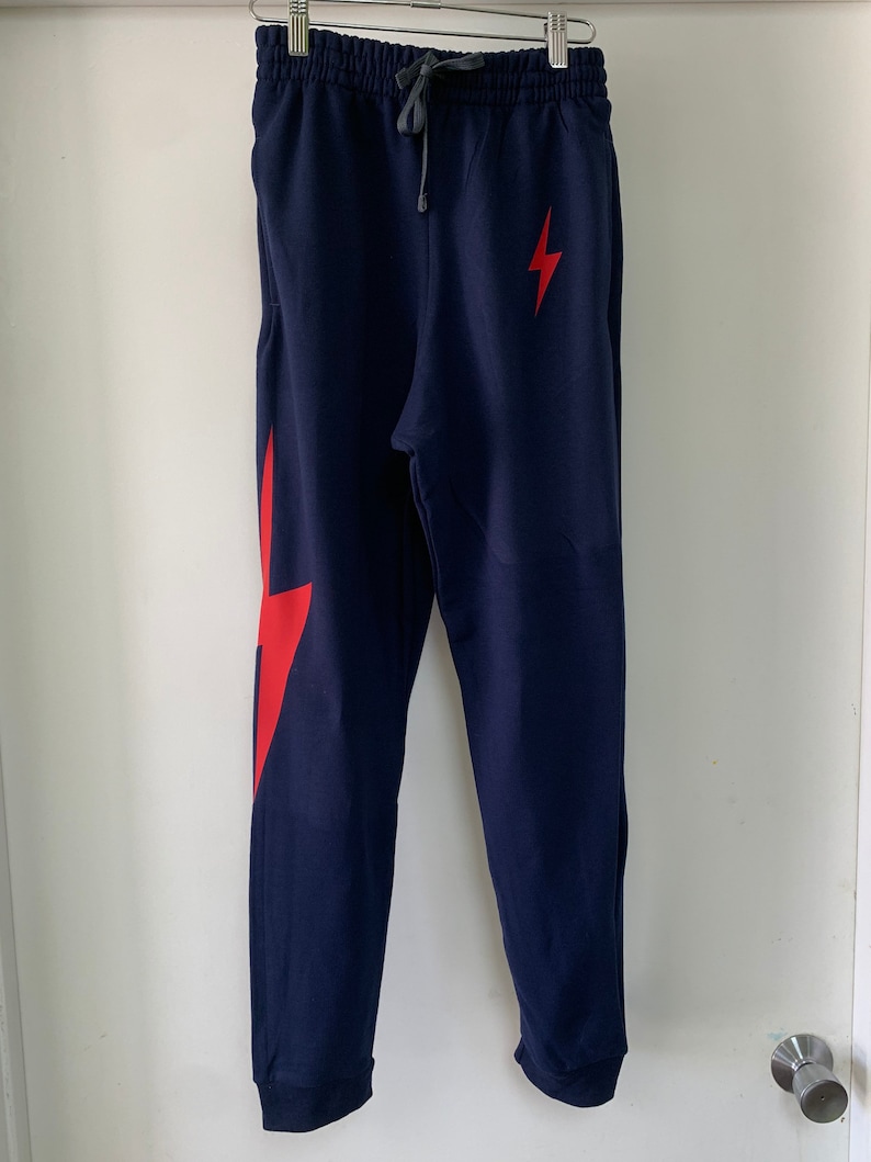 Puede incluir: Pantalones de ch&aacute;ndal azul marino con un gr&aacute;fico de rayo rojo en la pierna derecha. Los pantalones de ch&aacute;ndal tienen una cintura con cord&oacute;n y un dobladillo con pu&ntilde;os.