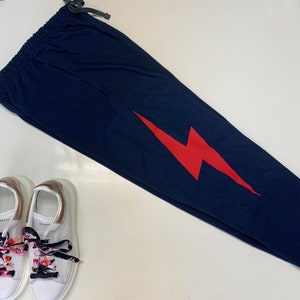 Puede incluir: Pantalones de ch&aacute;ndal azul marino con un gr&aacute;fico de rayo rojo. Los pantalones de ch&aacute;ndal tienen una cintura con cord&oacute;n.