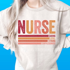 Peut inclure: Un sweat-shirt beige avec le mot "NURSE" en lettres rouges, orange et roses. Sous le mot "NURSE" se trouvent quatre bandes horizontales dans des tons de rouge, orange et rose. Les bandes portent les mots "CARING", "LOYAL", "STRONG" et "COMPASSIONATE" &eacute;crits dessus.