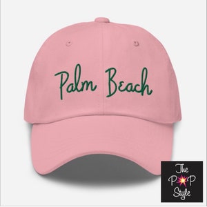 Op de afbeelding: Roze baseballpet met groene geborduurde tekst die "Palm Beach" zegt.