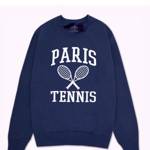 May include: Navy blue sweatshirt with the words "PARIS TENNIS" in white block letters and a graphic of crossed tennis rackets. The sweatshirt has a crew neck and long sleeves.