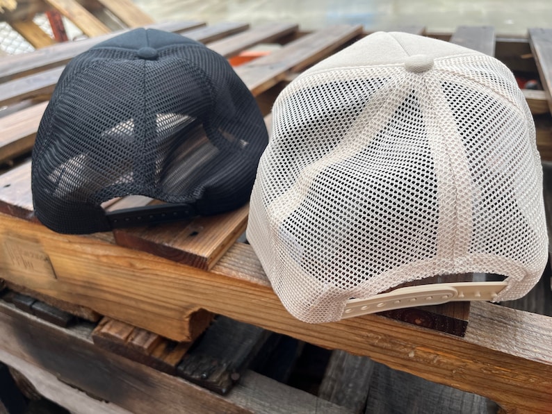 Puede incluir: Dos gorras de camionero de malla, una negra y otra beige. Ambas gorras tienen una malla en la parte posterior y un panel frontal s&oacute;lido.