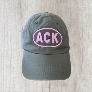 May include: A dark green baseball cap with a pink oval patch that says "ACK" on it.