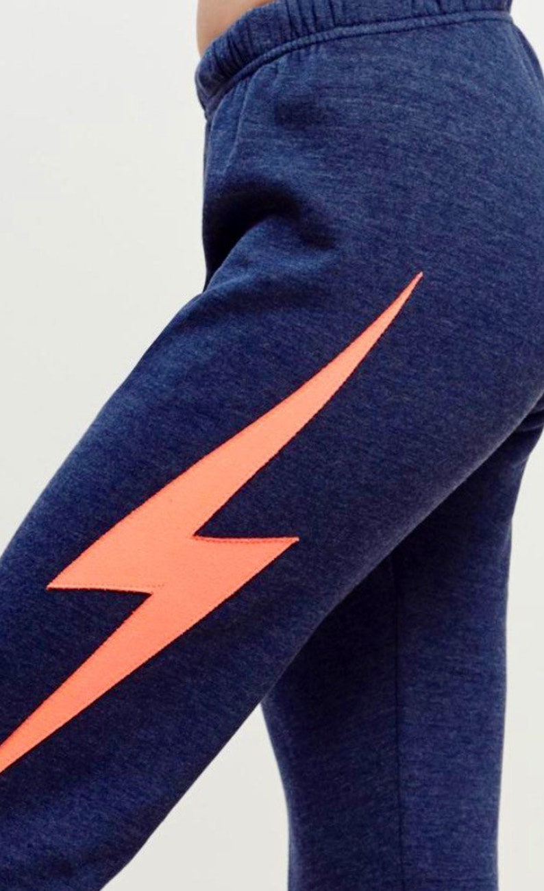 Puede incluir: Pantalones de ch&aacute;ndal azul marino con un gr&aacute;fico de rayo naranja brillante en la pierna izquierda.