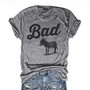May include: A heather grey t-shirt with a black graphic of a donkey and the word "Bad" in a retro font.
