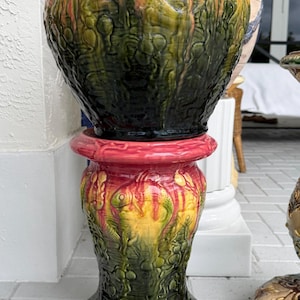 May include: A large, ornate ceramic planter with a pedestal base. The planter features a textured, glazed finish in shades of green, yellow, and red. The pedestal is a matching design, creating a cohesive and decorative piece for outdoor or indoor use.