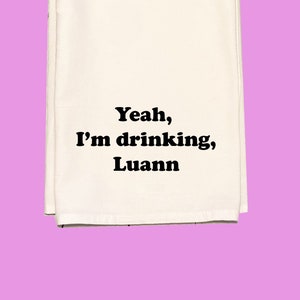 May include: White kitchen towel with black text that reads "Yeah, I'm drinking, Luann".
