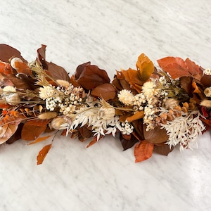 May include: A dried floral garland with brown and white flowers and leaves. The garland is perfect for adding a touch of fall to your home decor.