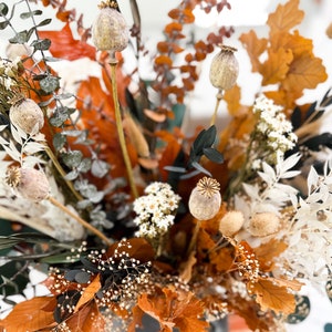 K&ouml;nnte beinhalten: Getrocknete Blumenarrangement mit braunen, wei&szlig;en und gr&uuml;nen Bl&auml;ttern. Die Anordnung enth&auml;lt getrocknete Mohnkapseln, Eukalyptusbl&auml;tter und wei&szlig;e getrocknete Blumen.