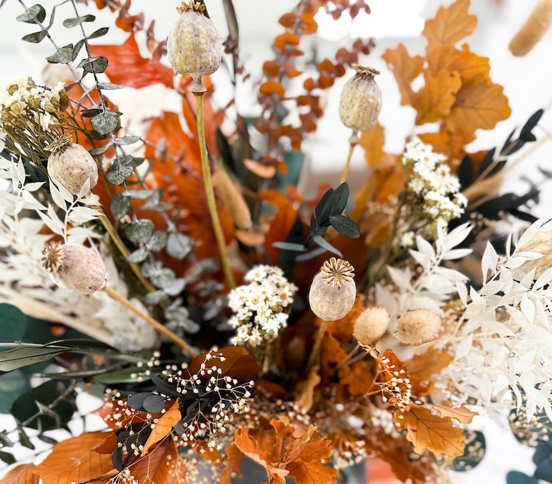 K&ouml;nnte beinhalten: Getrocknete Blumenarrangement mit braunen, wei&szlig;en und gr&uuml;nen Bl&auml;ttern. Die Anordnung enth&auml;lt getrocknete Mohnkapseln, Eukalyptusbl&auml;tter und wei&szlig;e getrocknete Blumen.