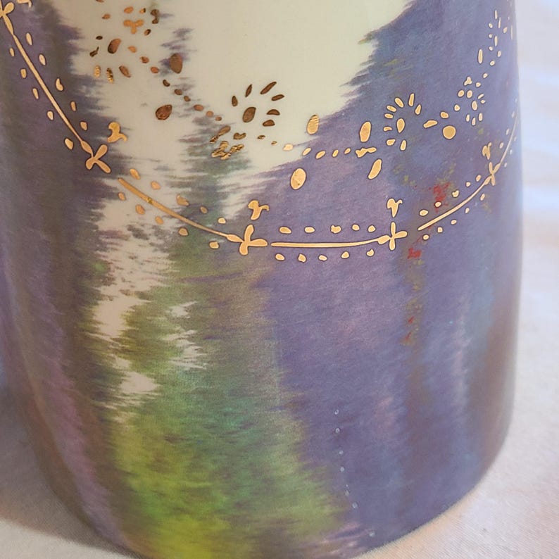 May include: A ceramic mug with a purple, green, and white tie-dye pattern. The mug has a gold design around the top.