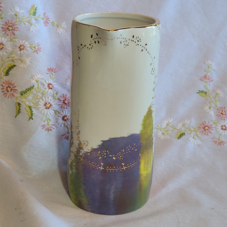 May include: A white ceramic pitcher with a gold rim and floral design. The pitcher has a watercolor-like design of purple, green, and yellow.