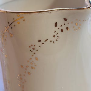May include: A white ceramic pitcher with a gold rim and delicate gold floral designs.